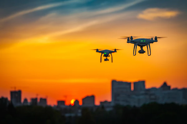 Drones sobrevoando horizonte urbano ao pôr do sol.